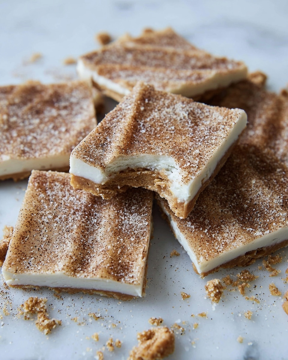 The image shows several square pieces of a dessert with two visible layers: a smooth, light beige bottom layer that looks soft and filled, topped with a thinner, slightly rough, light brown layer covered in sugar and cinnamon specks. The squares are stacked and scattered over a piece of crumpled parchment paper on a white marbled surface. Some crumbs and broken bits of the dessert are scattered around, adding texture and detail to the scene. photo taken with an iphone --ar 4:5 --v 7