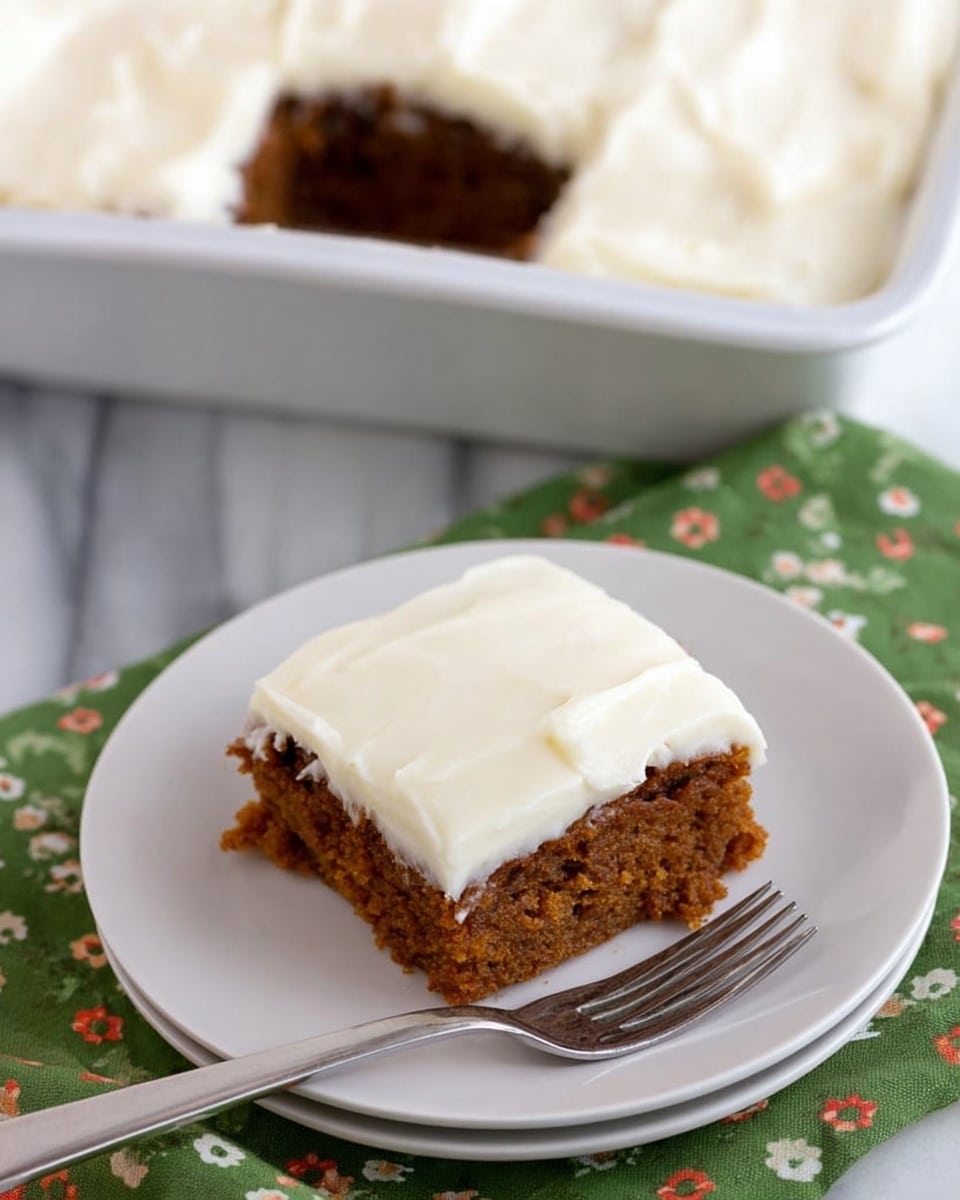 A square piece of cake sits on a white plate, showing two layers: a thick, rough-textured brown base and a smooth, creamy white frosting layer on top. The cake looks moist and crumbly, with the frosting evenly spread, creating a soft contrast. The plate rests on a green cloth with small white and red floral patterns. Next to the plate is a silver fork. In the background, a white pan with the same cake inside has one missing piece, with white frosting covering the entire top. All items are placed on a white marbled surface. Photo taken with an iphone --ar 4:5 --v 7