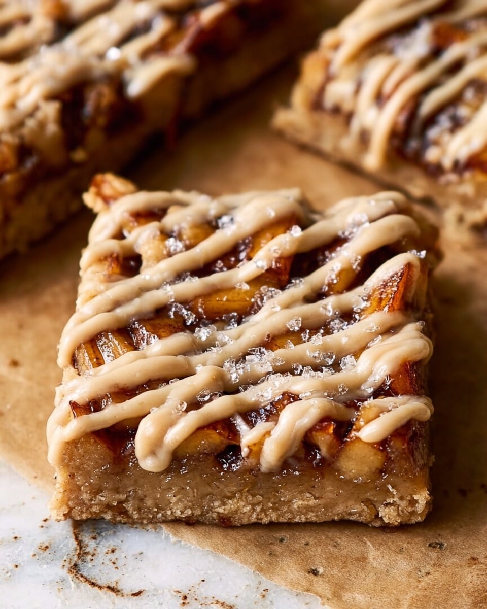 A close-up of a square dessert bar resting on parchment paper over a white marbled surface, showing two main layers: the bottom layer is a dense, golden-brown base with a soft texture, while the top layer has chunks of baked fruit and a slightly caramelized look in dark brown and amber tones. The entire bar is topped with thick, creamy, light beige drizzle in uneven lines, giving it a rich and smooth appearance with some sparkling sugar crystals scattered on top. Photo taken with an iphone --ar 4:5 --v 7