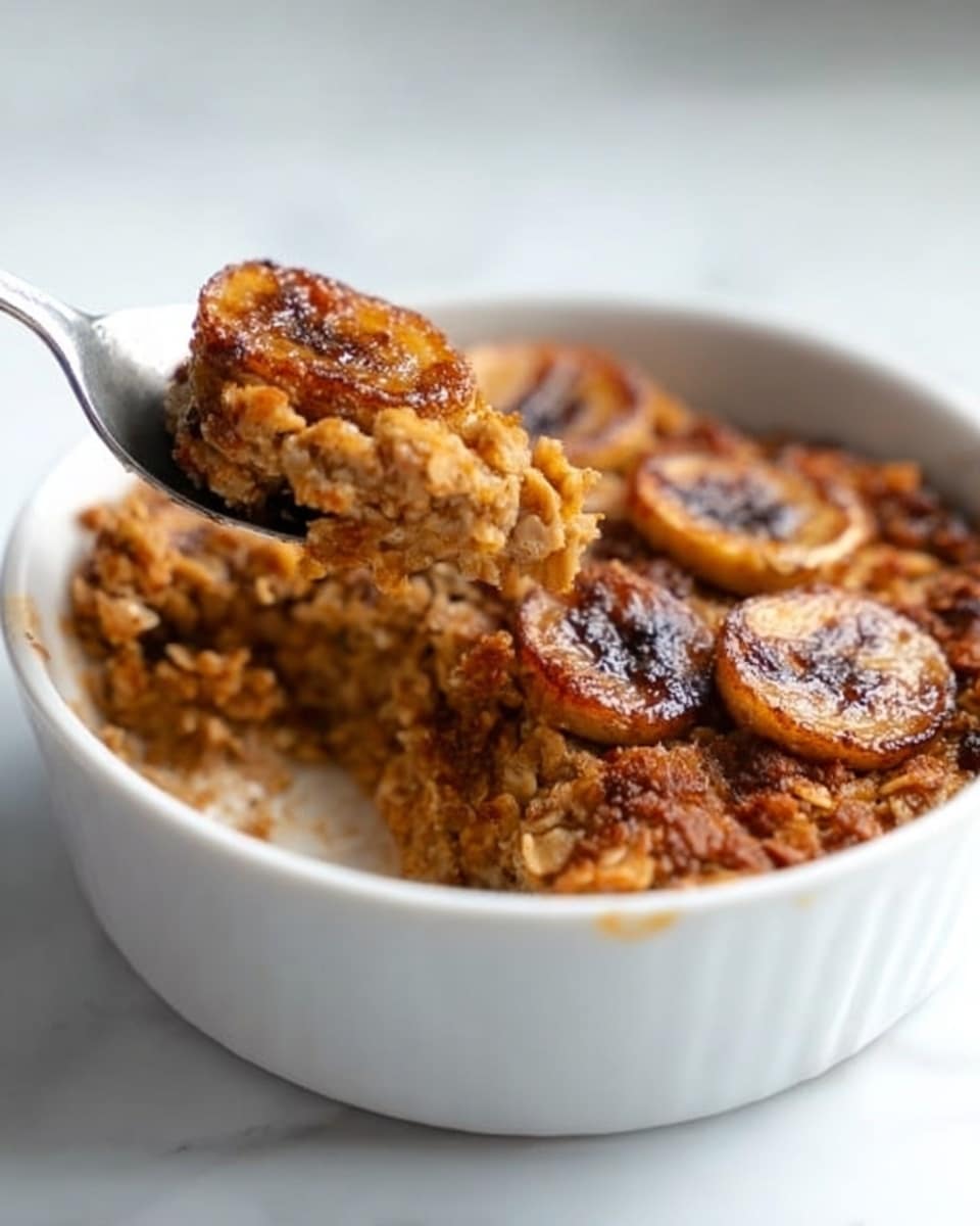 The image shows a white bowl with a warm baked oatmeal dish inside. The oatmeal is golden brown with a rough, crumbly texture. Sliced bananas cooked into the oatmeal add a darker brown color on top, and the edges look slightly crispy. A spoon is scooping some of the oatmeal with banana slices from the side. The bowl sits on a white marbled surface. Photo taken with an iphone --ar 4:5 --v 7