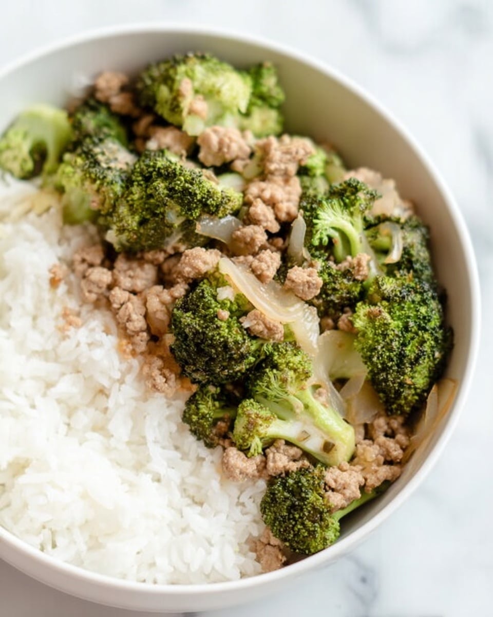 The image shows a white bowl filled with three layers of food. The bottom layer is white rice that looks soft and fluffy, placed on one side of the bowl. On top of the rice and covering the rest of the bowl are chunks of cooked green broccoli with a slightly textured surface. Mixed in with the broccoli are light brown, crumbly pieces of cooked ground meat, along with some translucent cooked onions. The bowl is placed on a white marbled surface, and the photo was taken with an iphone --ar 4:5 --v 7