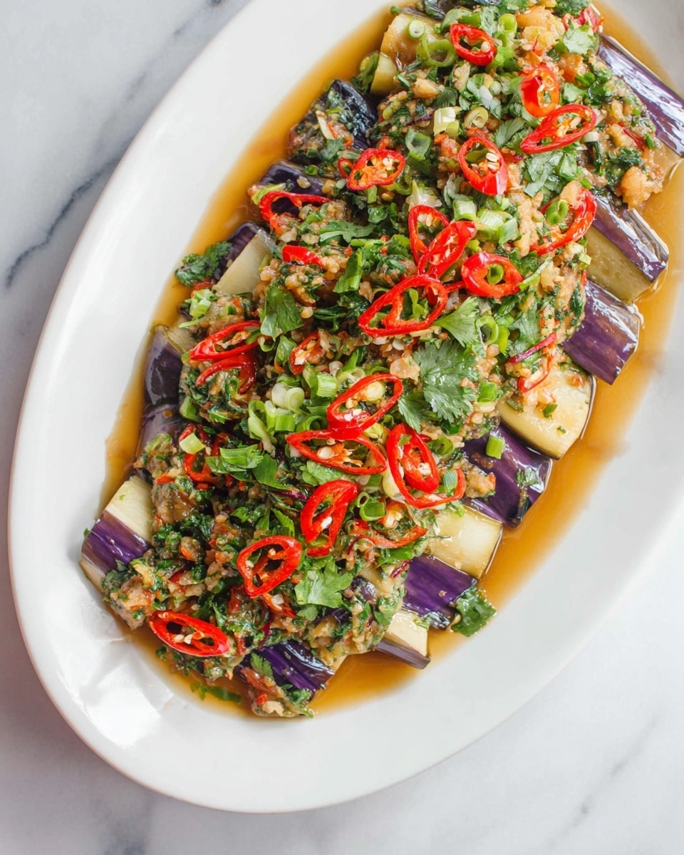 The dish is served on a large white oval plate, placed on a white marbled surface. The base layer consists of purple eggplant pieces arranged neatly across the plate. On top of the eggplant is a mixture of finely chopped green herbs, red chili slices, and small bits of garlic, all coated in a light brown sauce that pools slightly around the edges. The colors are vibrant, with the deep purple of the eggplant contrasting with the bright red chilies and fresh green herbs, making the dish look fresh and flavorful. photo taken with an iphone --ar 4:5 --v 7
