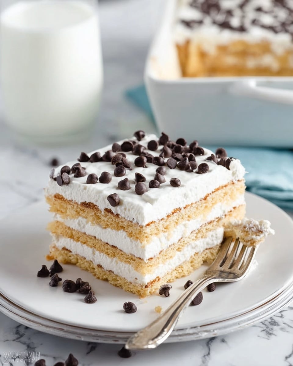 The image shows a square dessert in a silver baking pan on a white marbled surface. The dessert has four visible layers of light brown cake alternating with three layers of white cream. The top layer is covered with smooth white cream and sprinkled evenly with small dark chocolate chips. A slice has been taken out, revealing the neat layers inside. Photo taken with an iphone --ar 4:5 --v 7