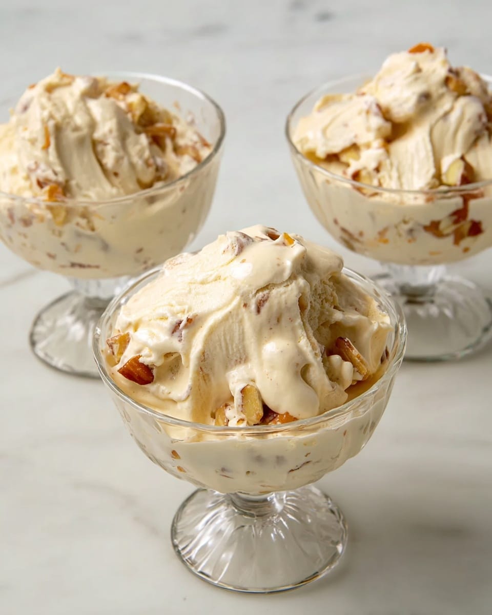 The image shows three clear glass dessert bowls filled with a creamy, light beige dessert mixed with chunks of light-colored fruit or nuts that add texture and small patches of light brown within the creamy layer. The bowls are placed on a smooth, white marbled surface, with one bowl in the front center and two slightly behind on each side. The dessert looks soft and thick with a swirled, slightly uneven top on each bowl that shows the creamy and chunky mix clearly. photo taken with an iphone --ar 4:5 --v 7