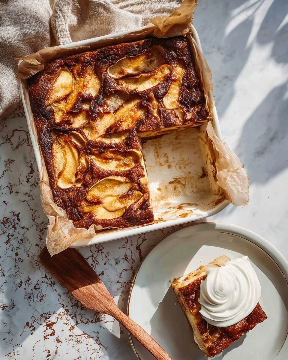 The image shows a square apple dessert in a white baking dish lined with parchment paper, with a piece already removed. The dessert has two main layers: the bottom layer is a brown, slightly crispy crust, and the top layer is golden with baked apple slices that have darker browned spots, creating a textured look. Next to the baking dish, there is a white plate with one piece of the dessert served alongside a swirl of white cream. A wooden spatula with some crumbs rests nearby on a white marbled surface with rustic patterns. Light and shadows give a natural feel to the setup. Photo taken with an iphone --ar 4:5 --v 7