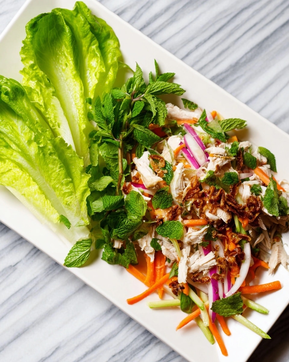 A white rectangular plate holds a colorful salad arranged in two parts: on the left, several fresh green lettuce leaves with a bright and crisp texture; on the right, a mixed pile of thinly sliced white chicken pieces, orange carrot sticks, thin white and purple onion slices, and fresh green herbs like cilantro and mint, all topped with small crispy brown fried shallots. The plate is set on a white marbled surface. photo taken with an iphone --ar 4:5 --v 7