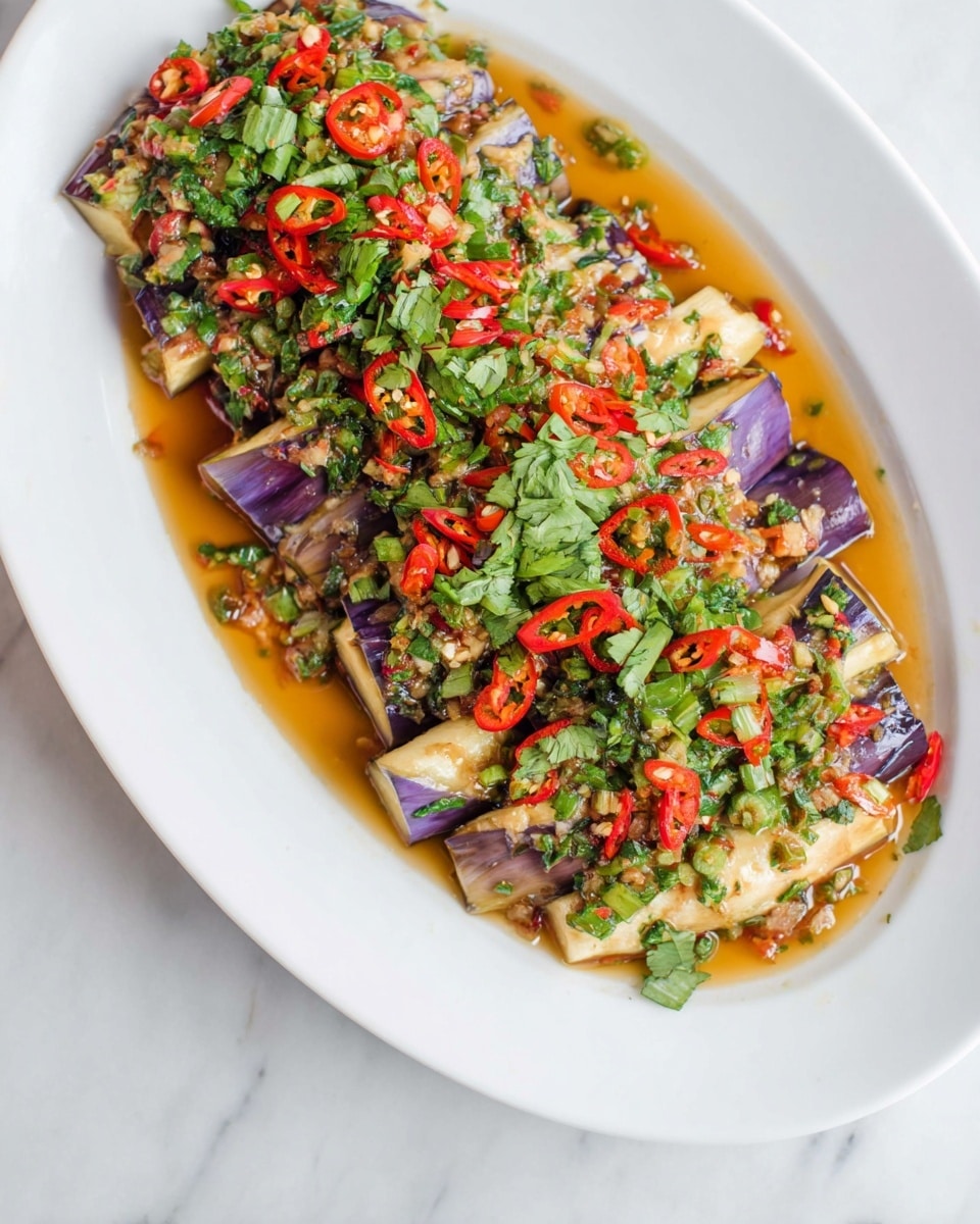 A white oval plate holds a colorful dish with several layers. At the bottom, there are soft, purple and white eggplant pieces, arranged close together. On top of the eggplant, thin slices of bright red chili peppers are scattered all over. Over the chili peppers, there are small chopped green onions mixed with fresh green herbs that look like cilantro. The dish is covered in a glossy, light brown sauce that pools slightly at the edges of the plate. The background shows a white marbled surface. Photo taken with an iphone --ar 4:5 --v 7
