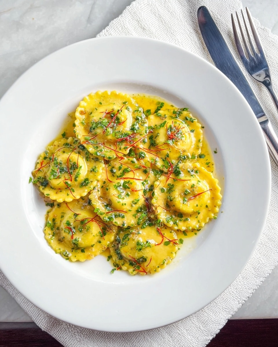 A white plate holds a serving of round ravioli with a ridged edge, coated in a yellow sauce that glistens and pools slightly on the plate. The ravioli are evenly spread out in a single layer, topped with finely chopped green herbs and thin strands of red saffron. The plate sits on a white marbled surface beside a white textured napkin with a silver fork and knife resting on it. The overall look is fresh with a mix of yellow, green, and red against the white plate and background. photo taken with an iphone --ar 4:5 --v 7